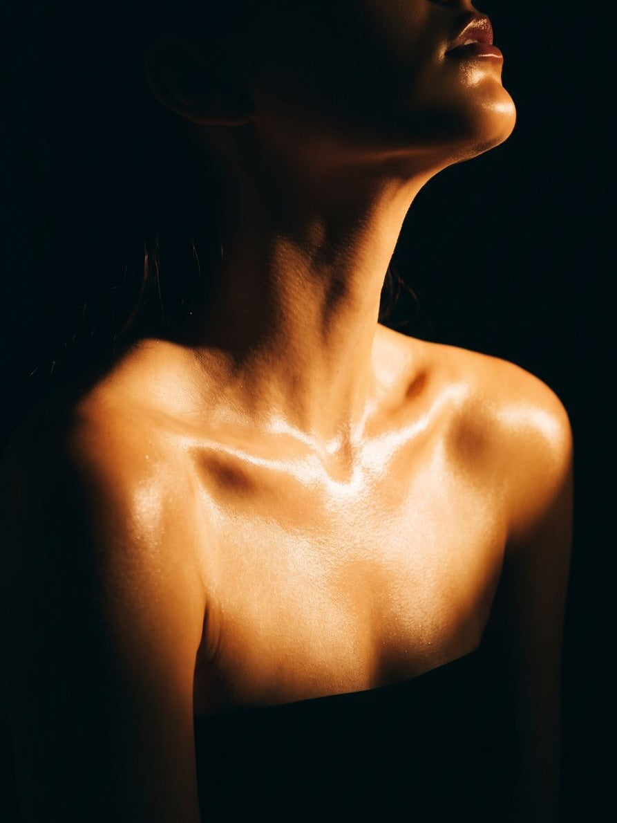 Chiaro- scuro photography Close-up of a woman's neck, shoulders, and upper chest in dramatic low-key lighting against a black background.